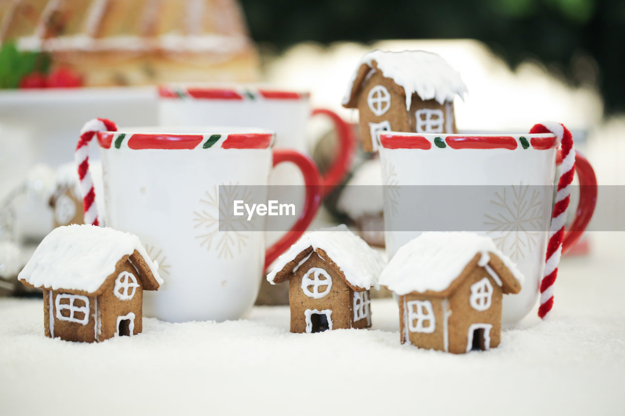 Close-up of gingerbread house and white mugs decorated on table during christmas