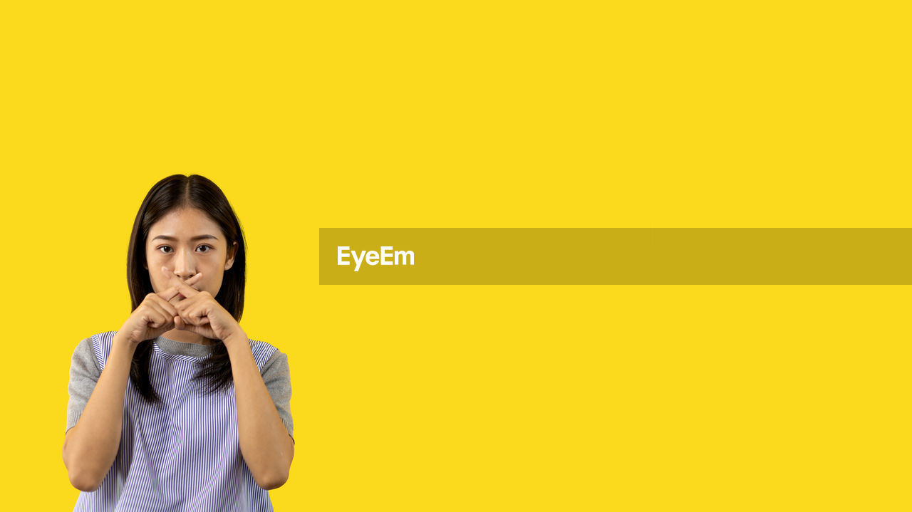 yellow, one person, copy space, studio shot, colored background, yellow background, portrait, women, adult, young adult, waist up, indoors, front view, looking at camera, emotion, smiling, happiness, standing, black hair, casual clothing, hairstyle, person, clothing, holding, long hair, cut out, female, human face, sign language