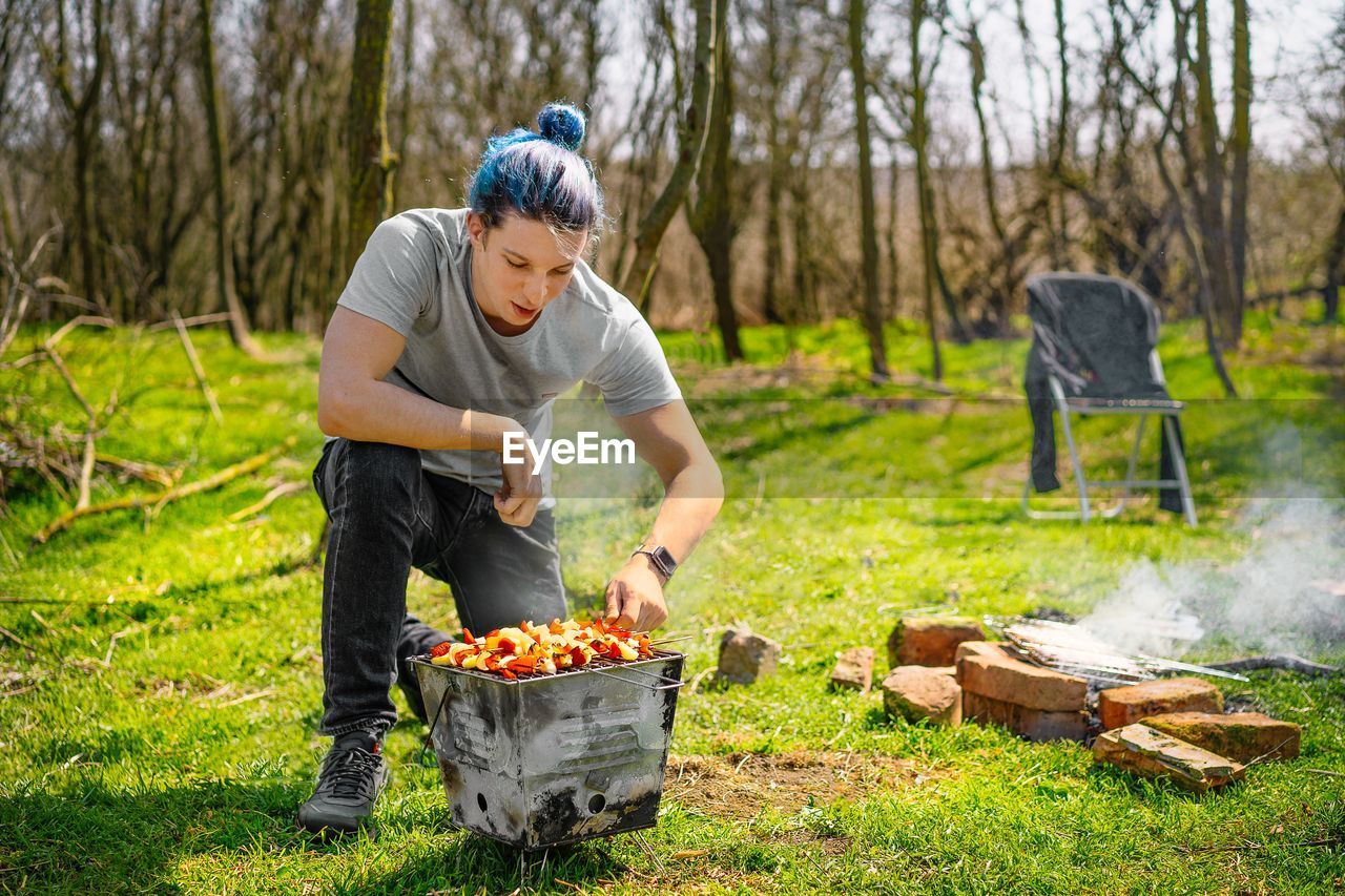 Young man preparing barbecue skewers in the forest during springtime