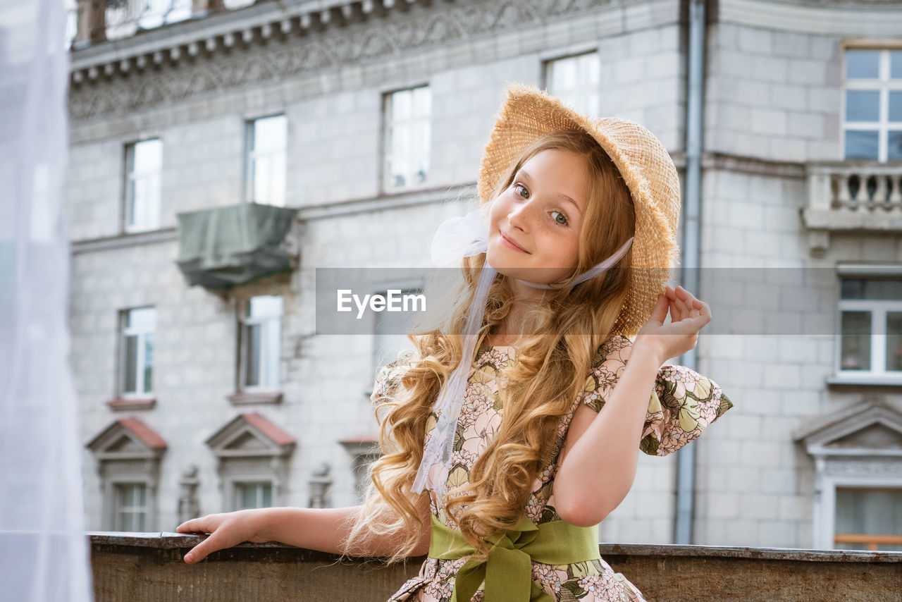 Little girl in dress and hat posing on the balcony