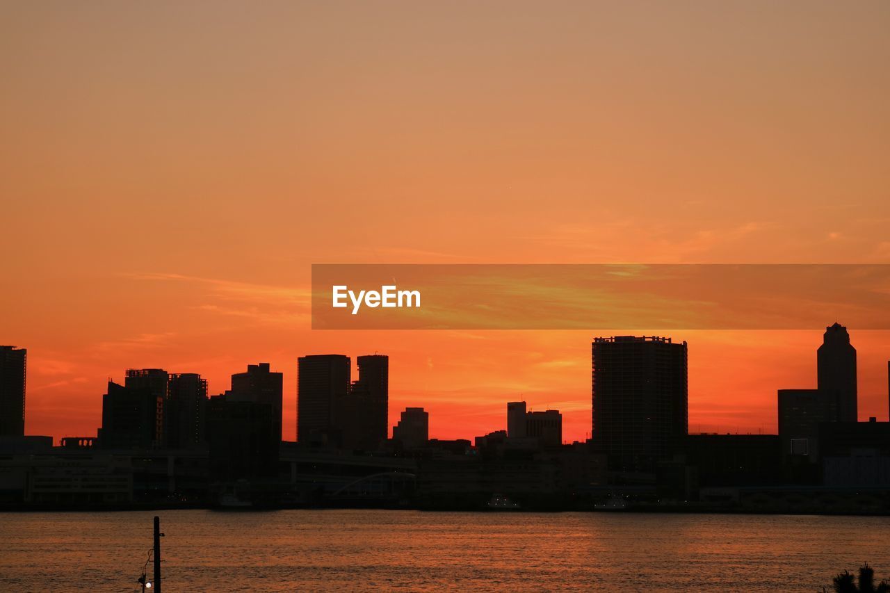 Silhouette buildings in front of calm sea at sunset