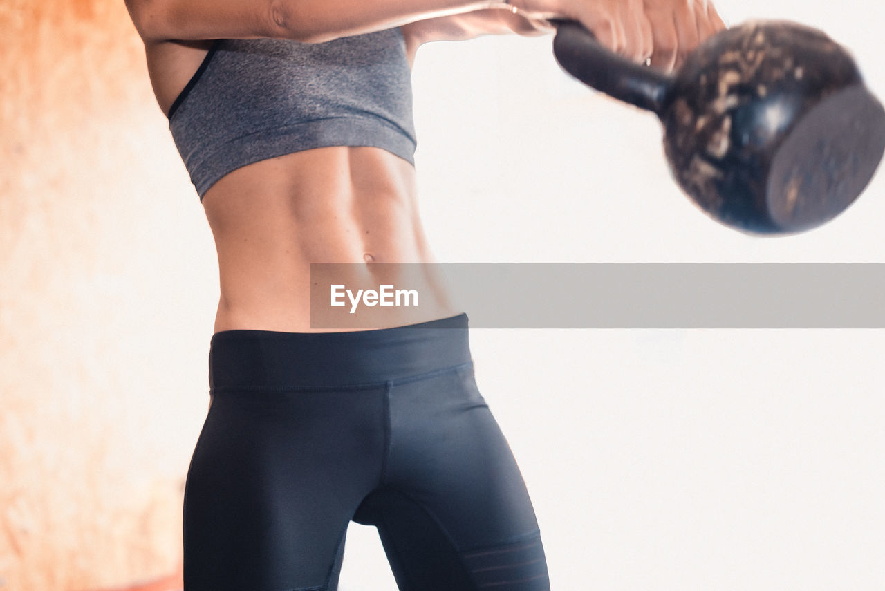 Midsection of young woman lifting kettlebell in gym