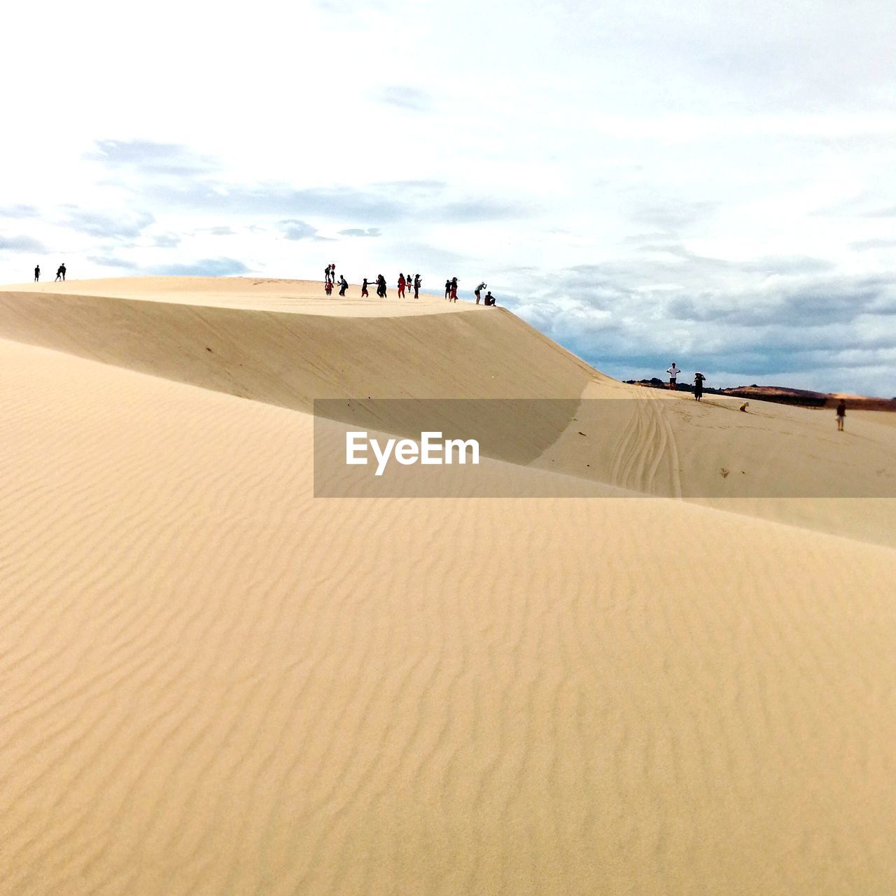 People on sand dune in desert against sky