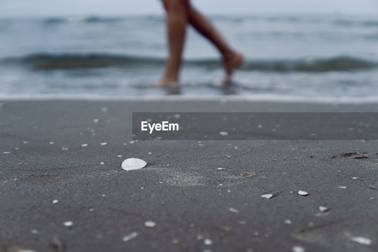 LOW SECTION VIEW OF WOMAN WALKING ON BEACH