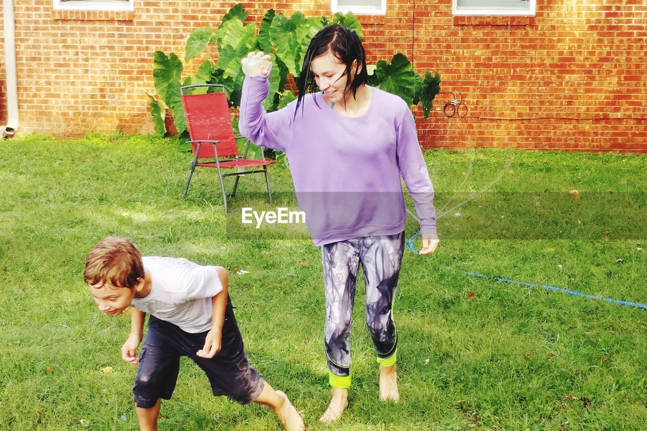 Full length of teenage girl with brother holding water bomb at lawn