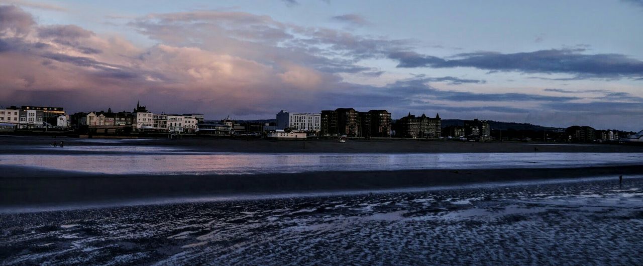 City at waterfront against cloudy sky