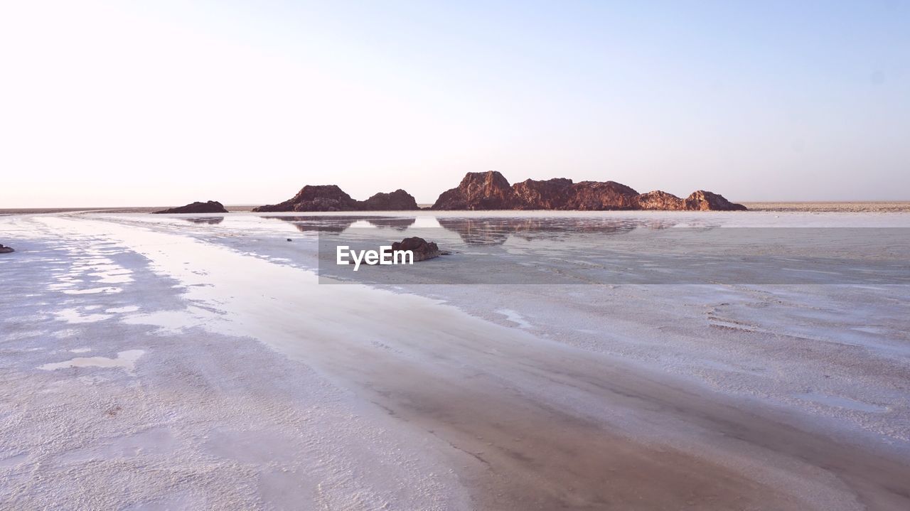 ROCKS ON BEACH AGAINST CLEAR SKY