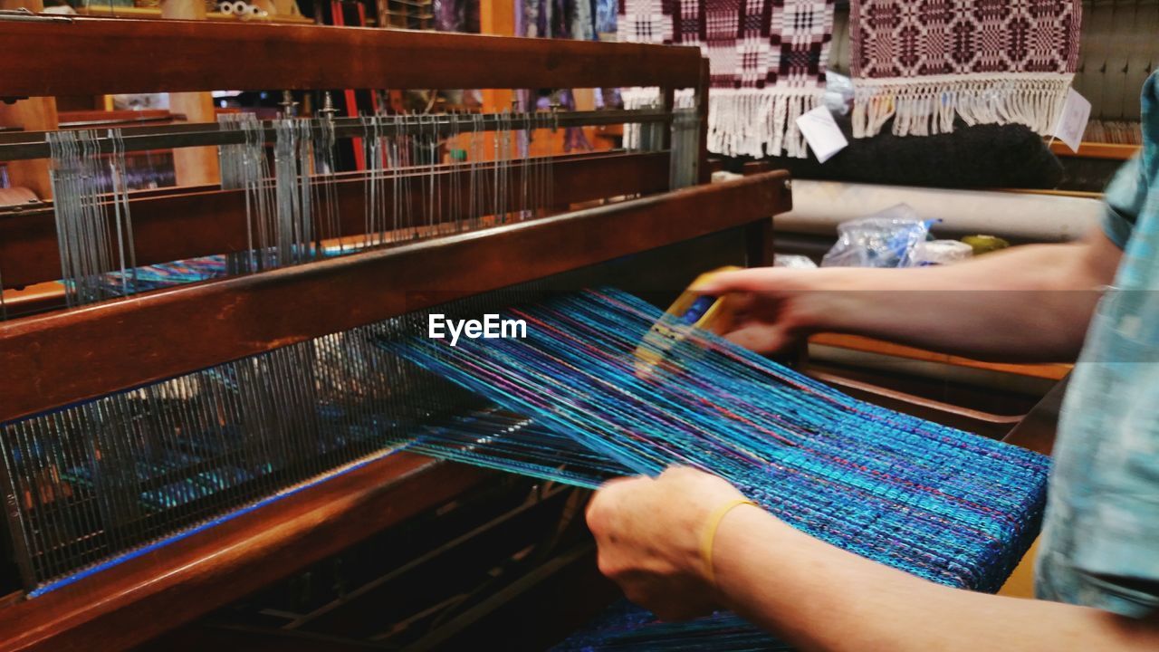 Midsection of woman weaving looms with shuttle at workshop