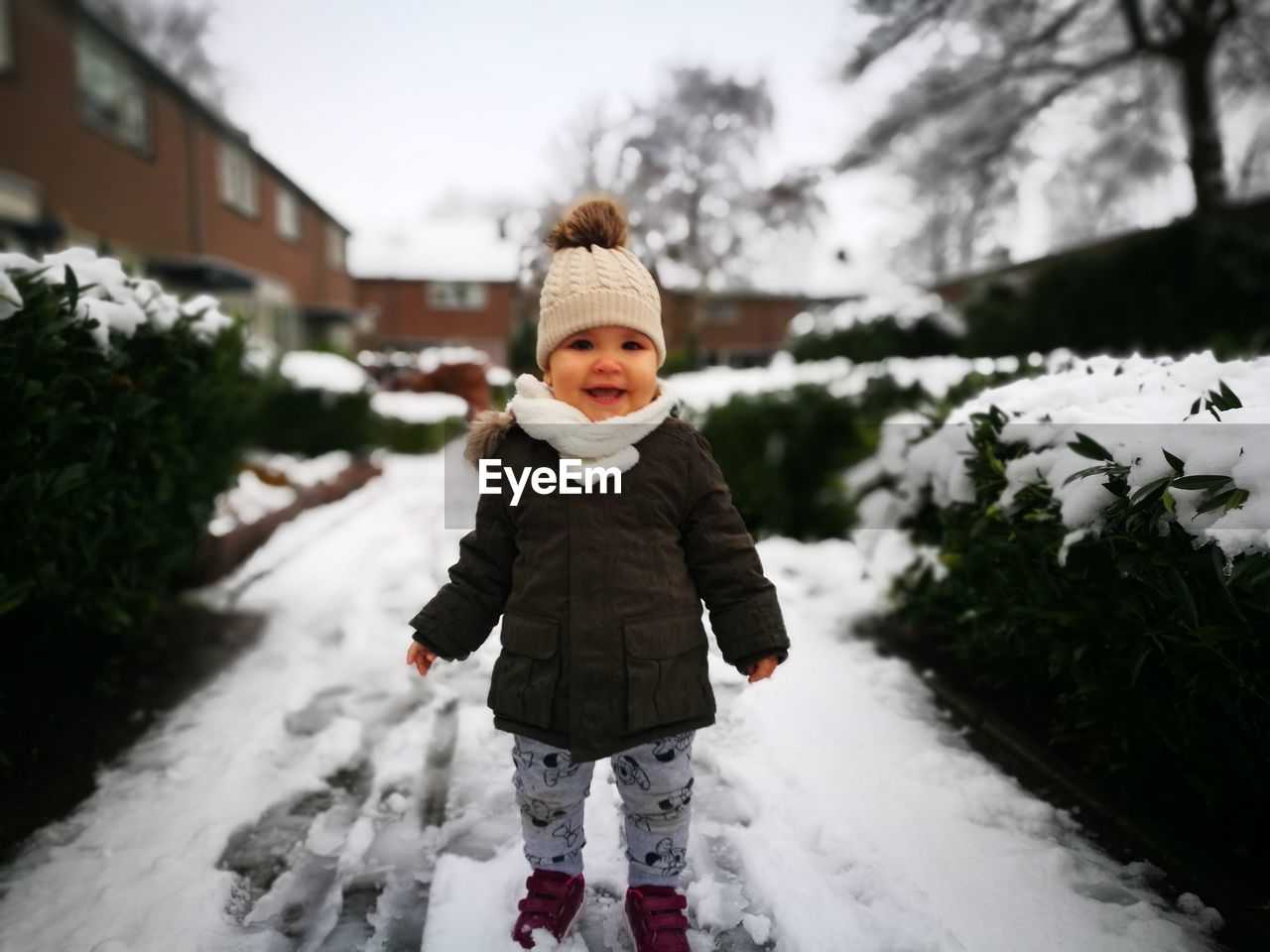 Full length portrait of cute cheerful baby girl wearing warm clothing while standing on snow