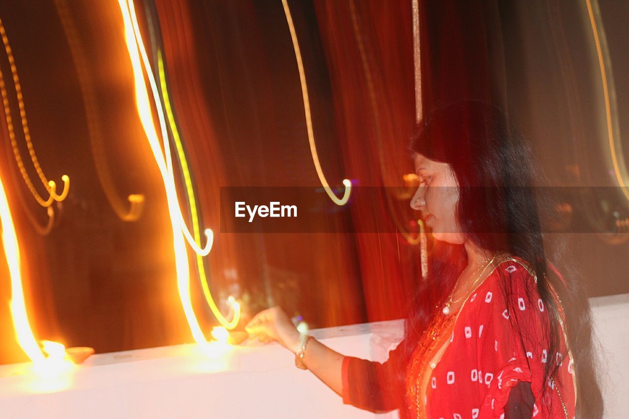 Woman igniting diya on retaining wall during diwali at night