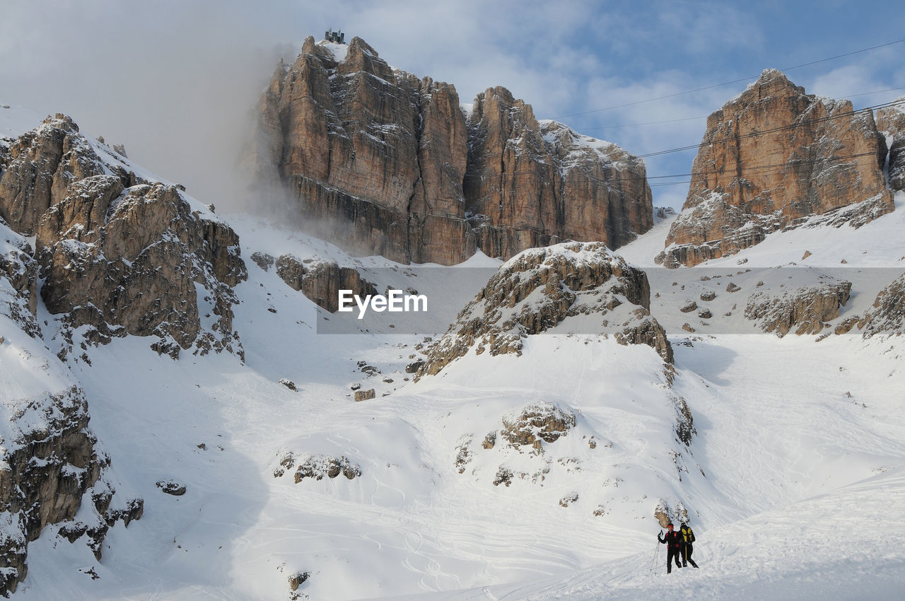 People climbing on snowcapped mountains against sky