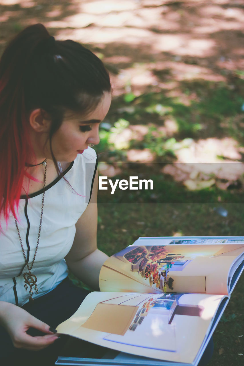 Woman looking at pictures on book while crouching at park