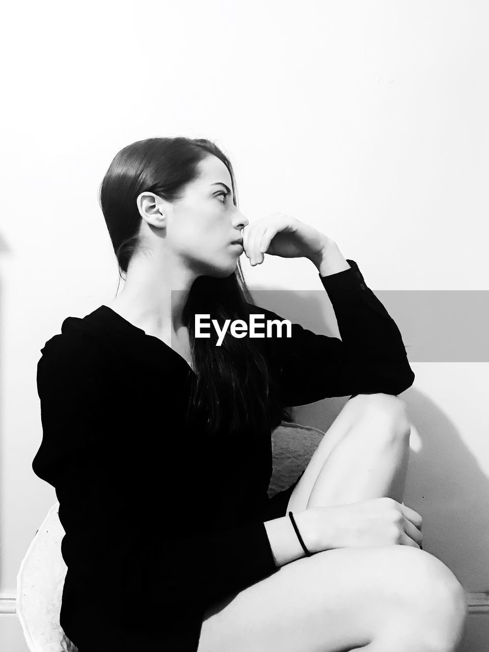 YOUNG WOMAN LOOKING AWAY WHILE SITTING ON WALL