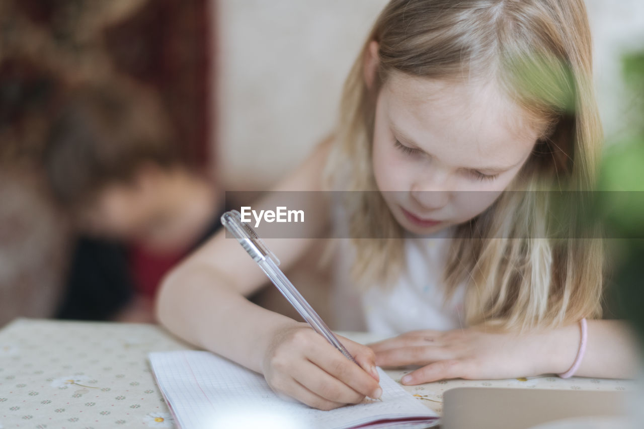 Blondie girl writing with pen while sitting on table