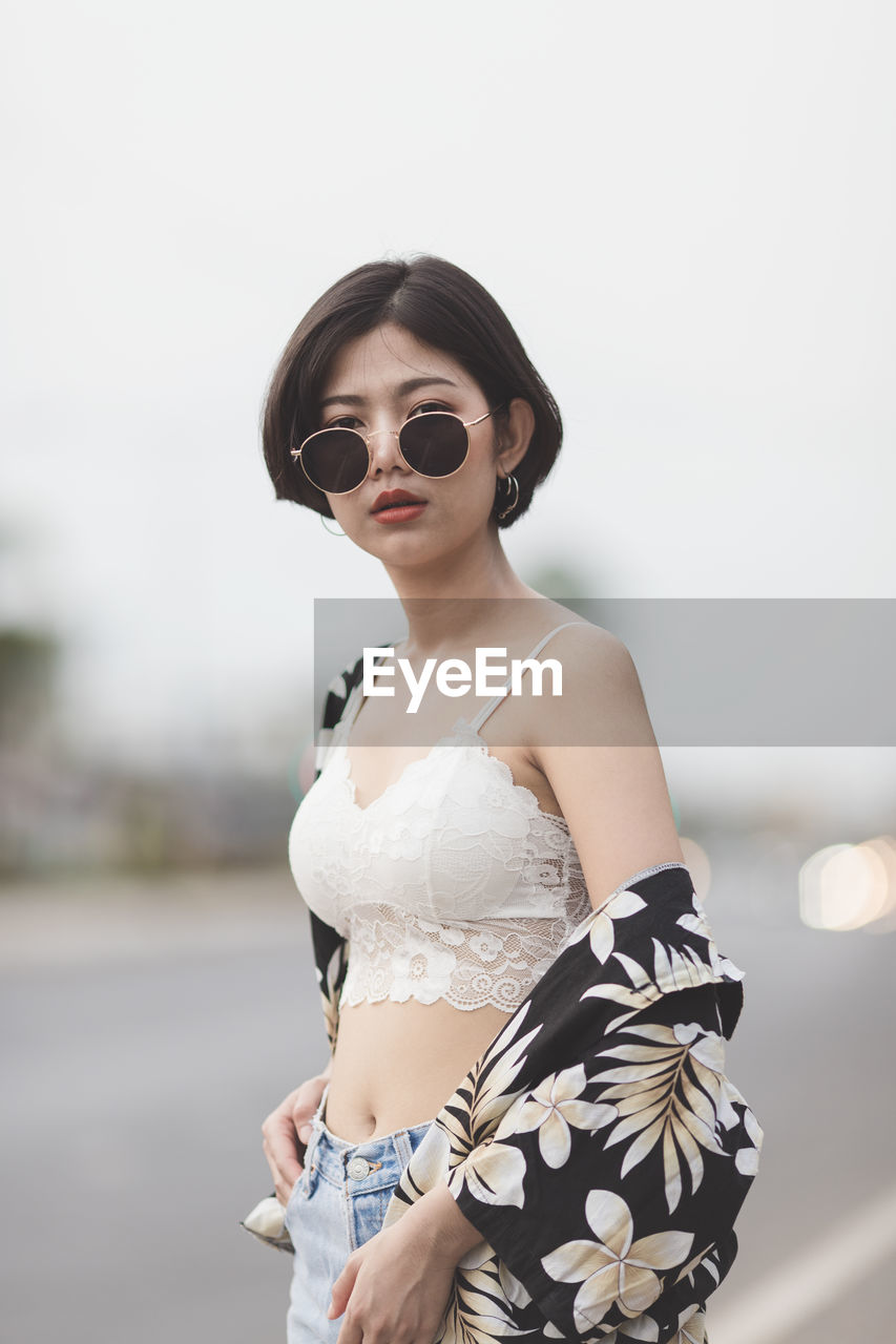 Portrait of sensuous young woman wearing sunglasses while standing on road