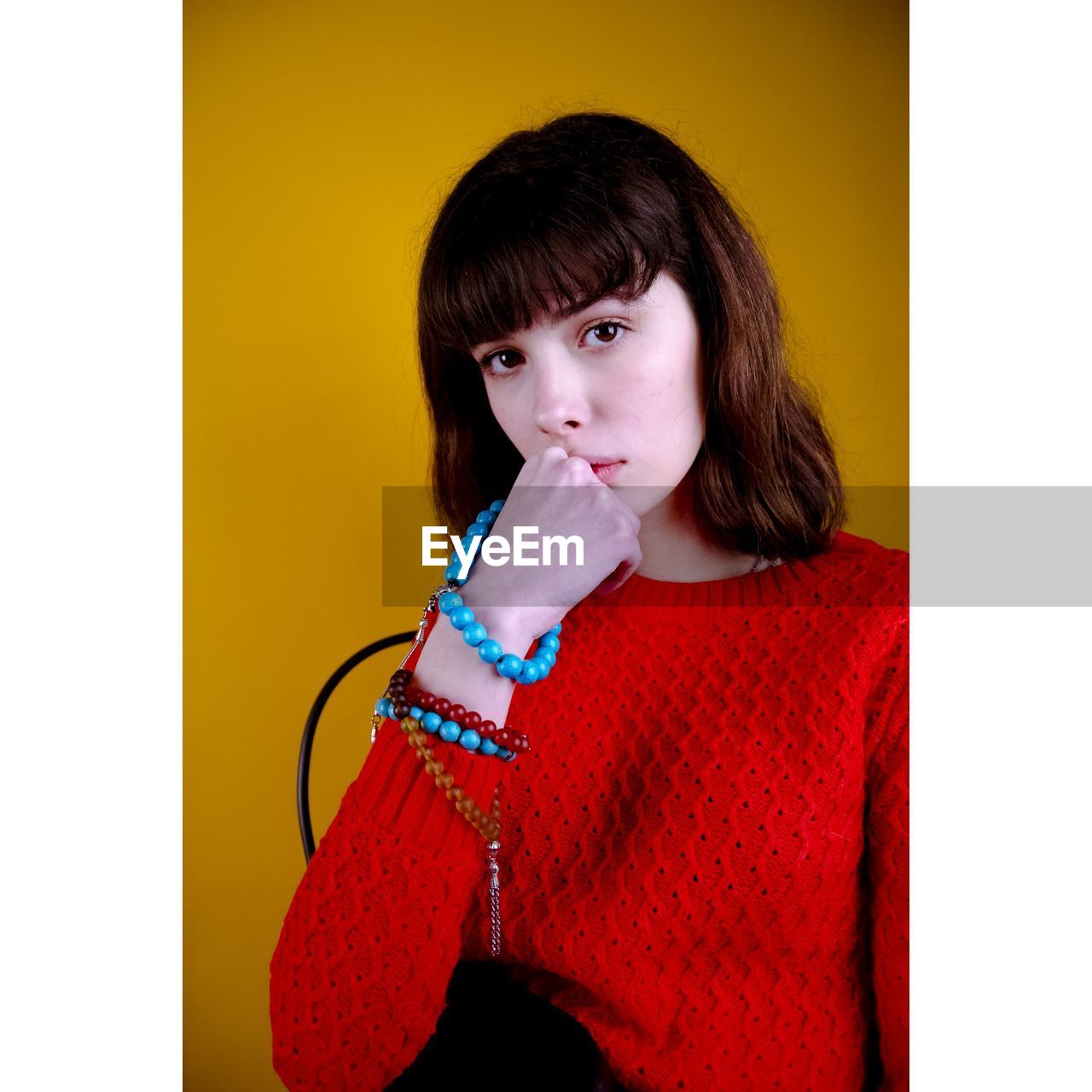 Portrait of beautiful young woman sitting against yellow background