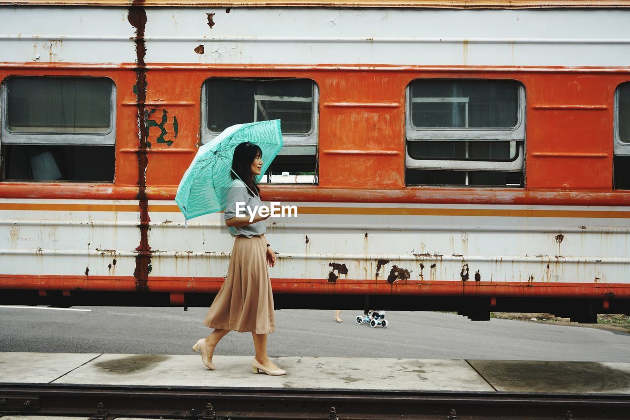 Side view of woman with umbrella walking at railroad station