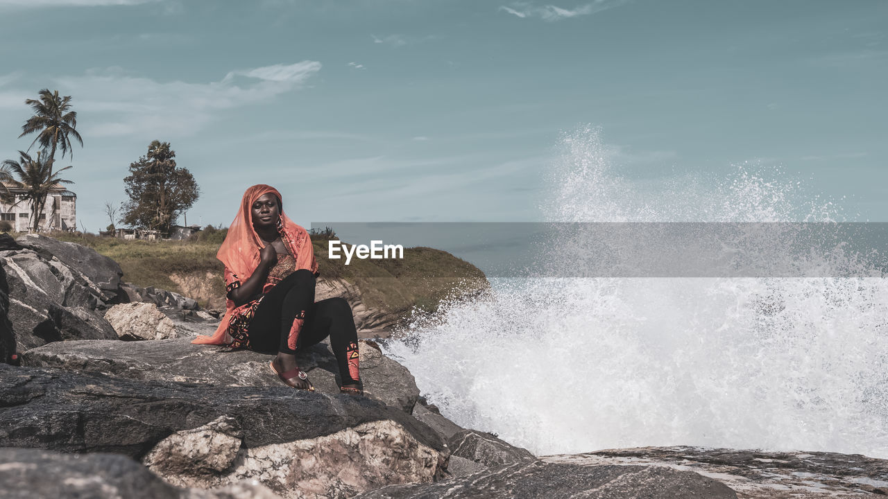 Full length of woman sitting on rock by sea