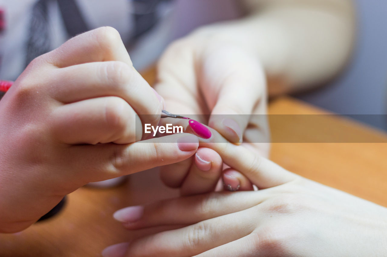 Cropped hands of woman painting friend fingernail at home