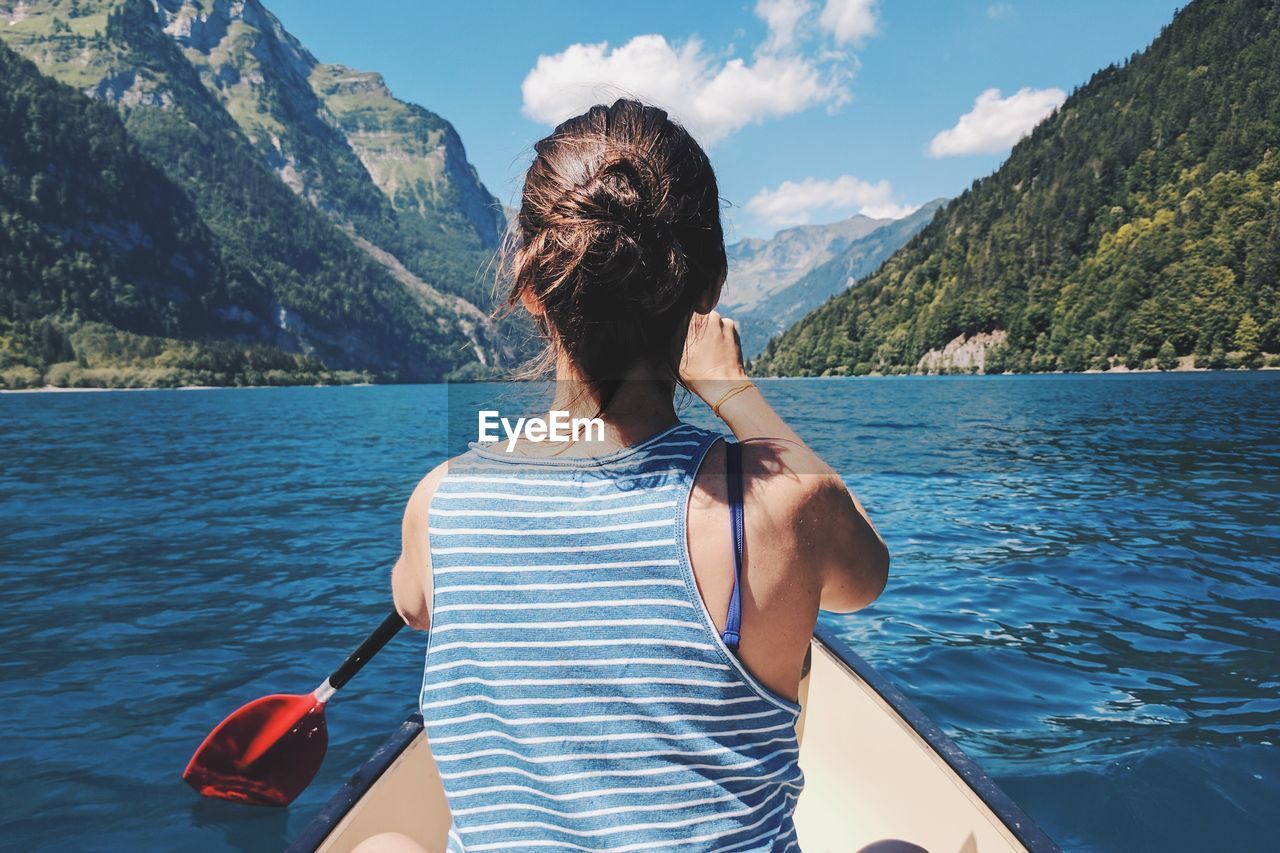 REAR VIEW OF WOMAN WITH UMBRELLA ON SHORE AGAINST MOUNTAINS