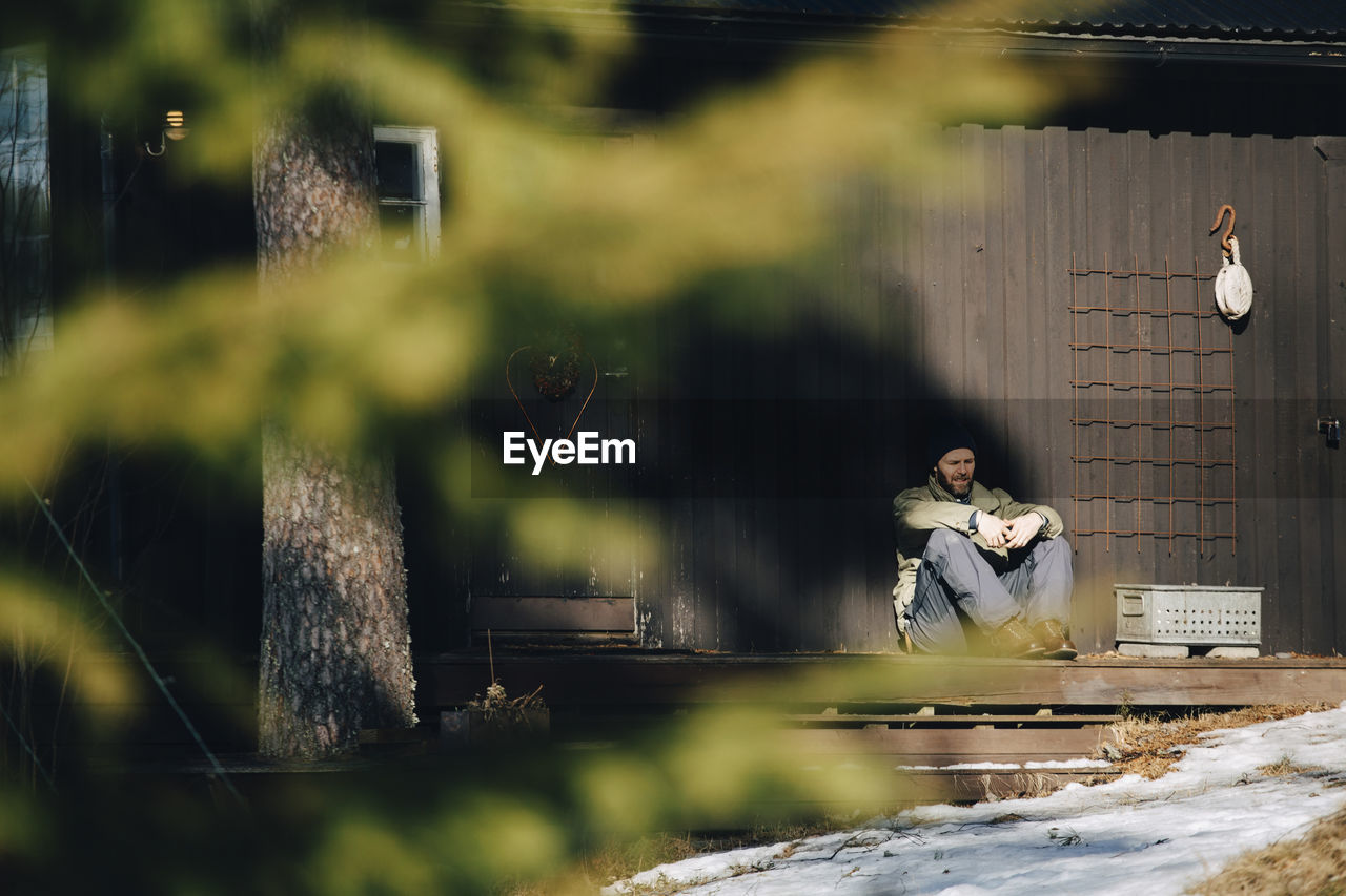 Mature man sitting on porch during sunny day in winter