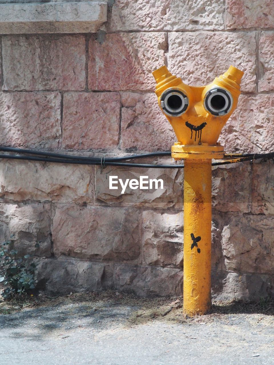 CLOSE-UP OF YELLOW FIRE HYDRANT AGAINST WALL