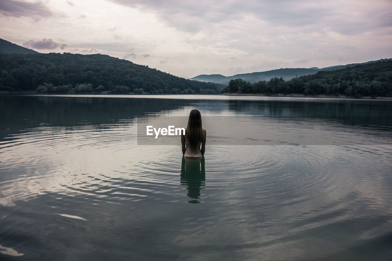 Young woman standing in lake against sky during sunset
