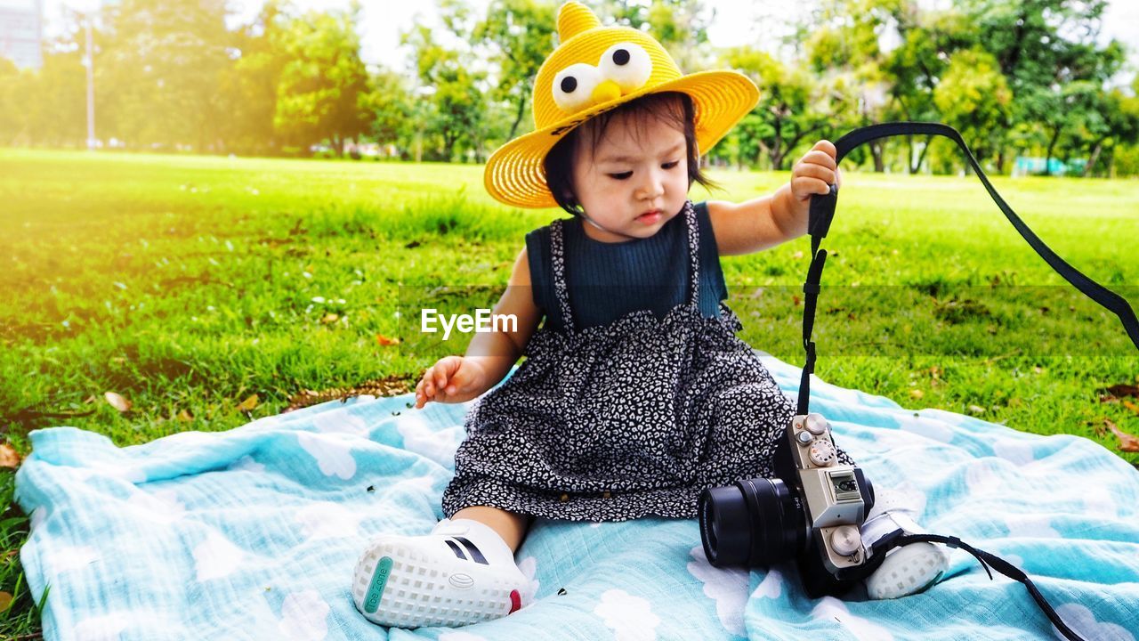 Baby girl playing with camera while sitting in park