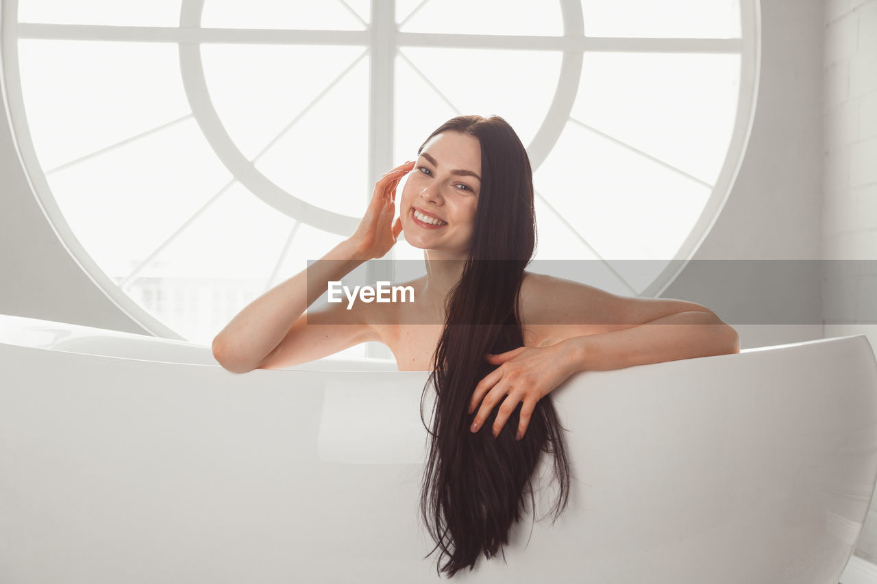 PORTRAIT OF BEAUTIFUL WOMAN STANDING AGAINST WINDOW