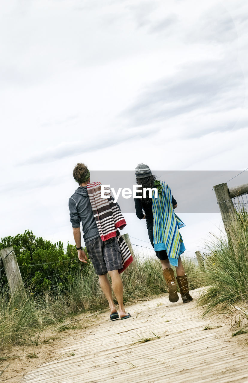 Tilt image of man and woman walking on pathway against cloudy sky