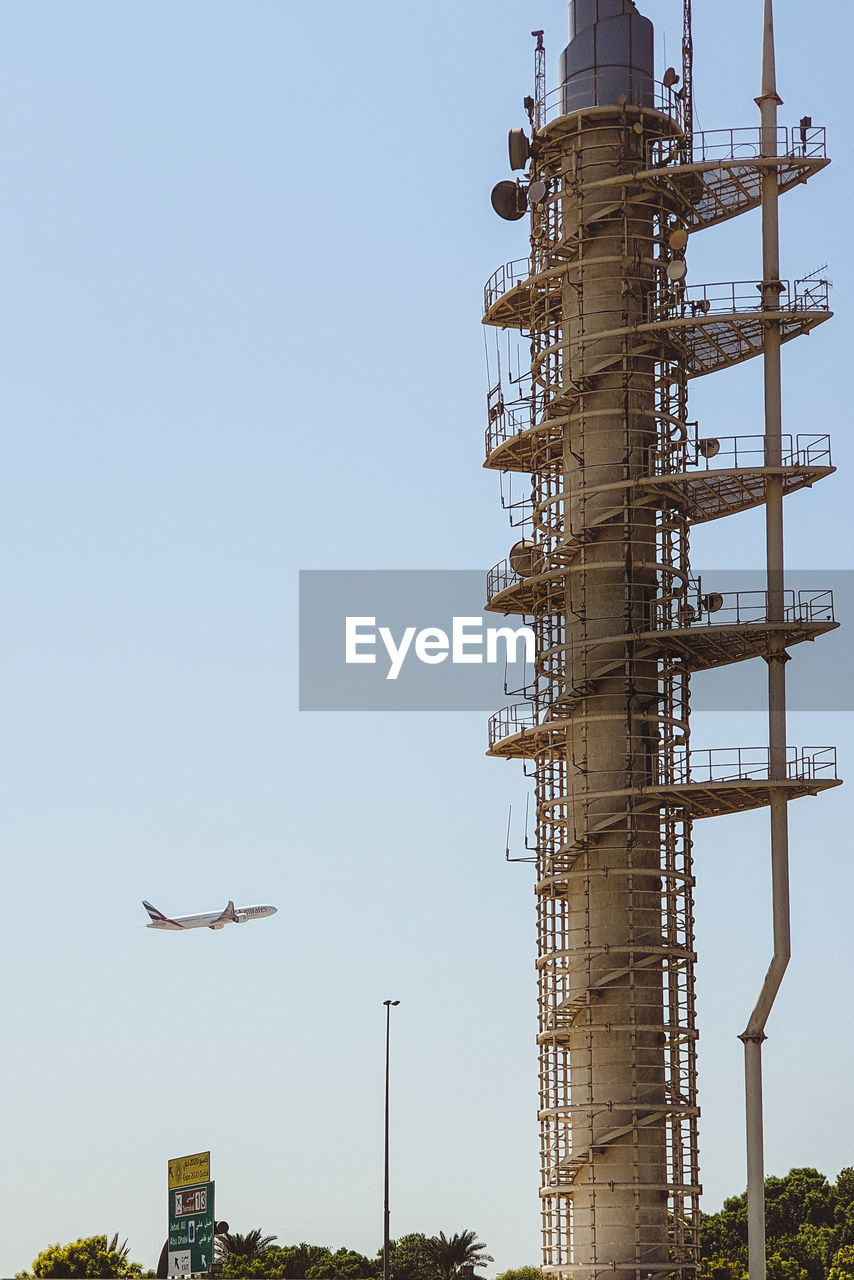 Low angle view of a  watchtower against clear sky and a flying airplane in dubai. 