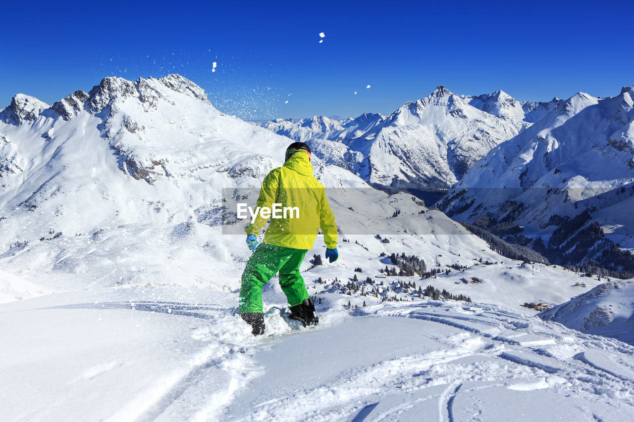 Rear view of man snowboarding on snowcapped mountain against sky