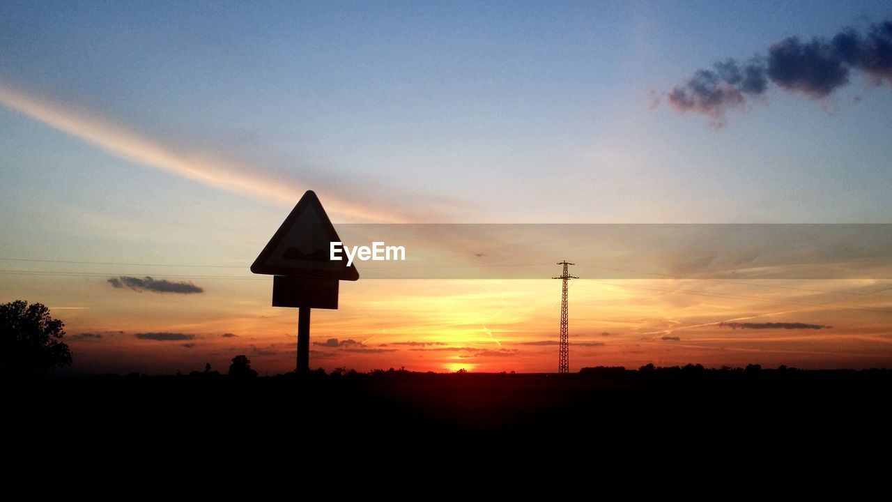 Silhouette signboard on field against sky during sunset