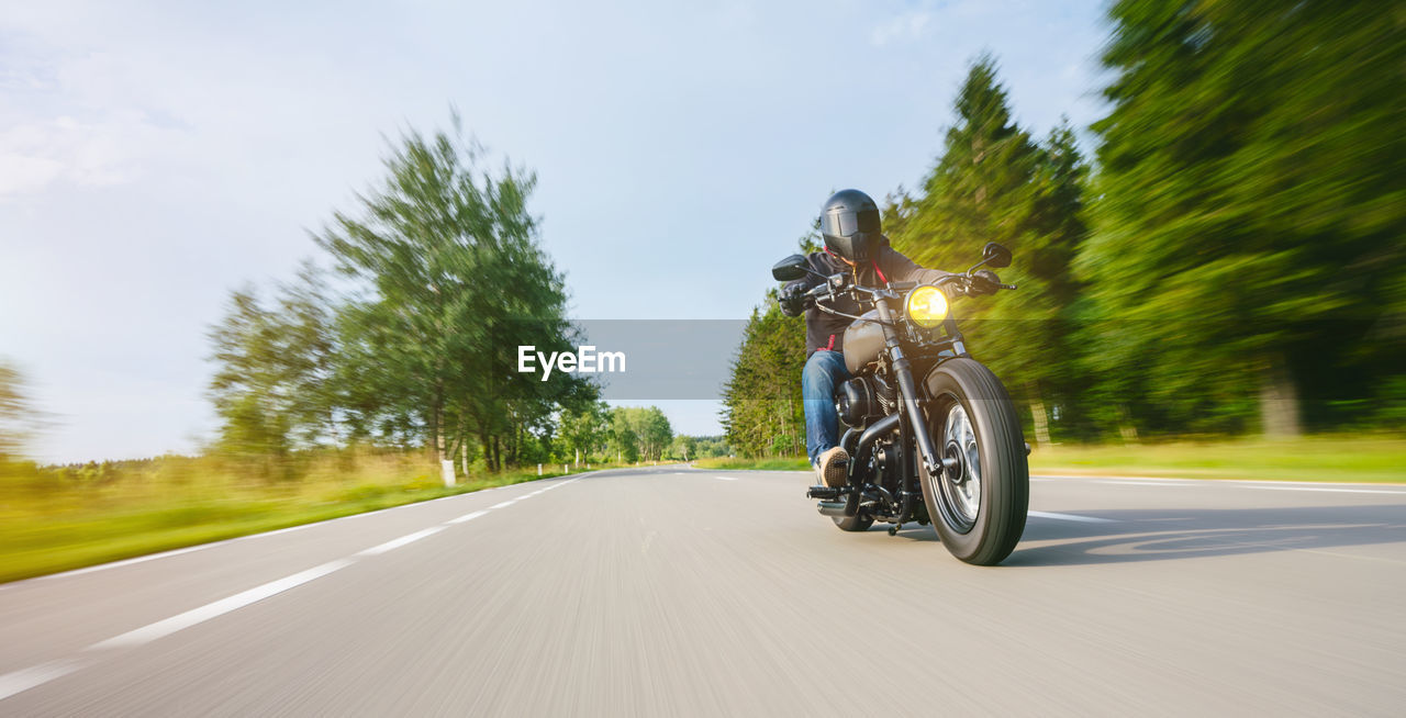 Man riding motorcycle on road amidst trees against sky