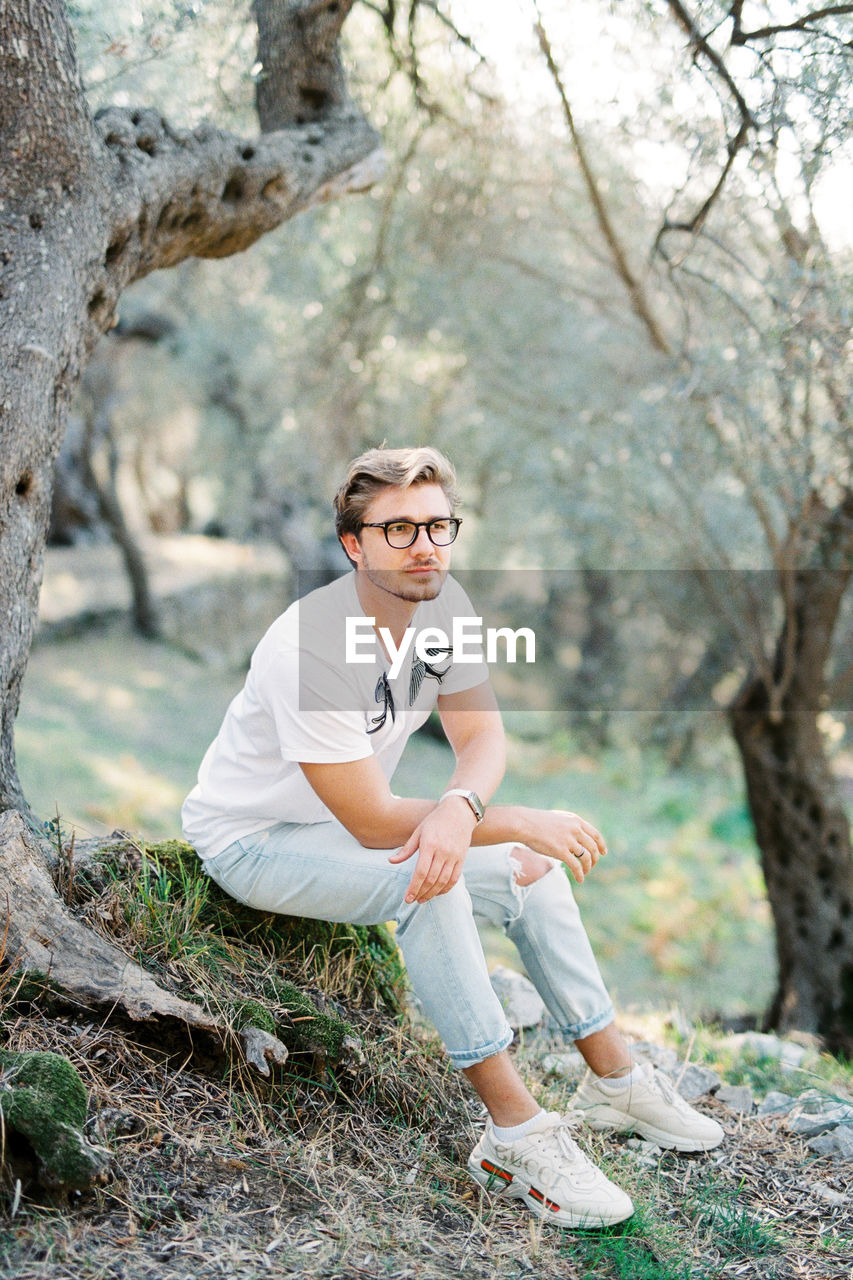 portrait of young man sitting on tree