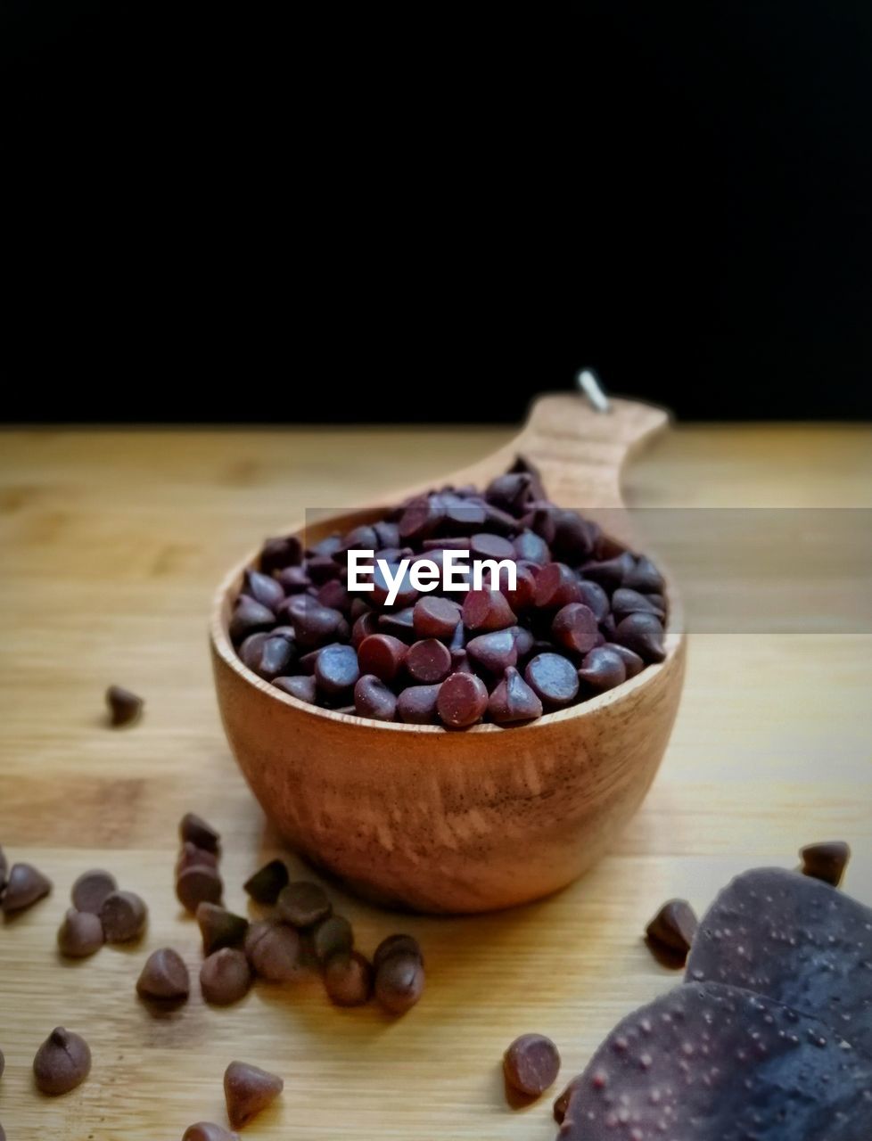 Close-up of chocolate chips in bowl on wooden table against black background