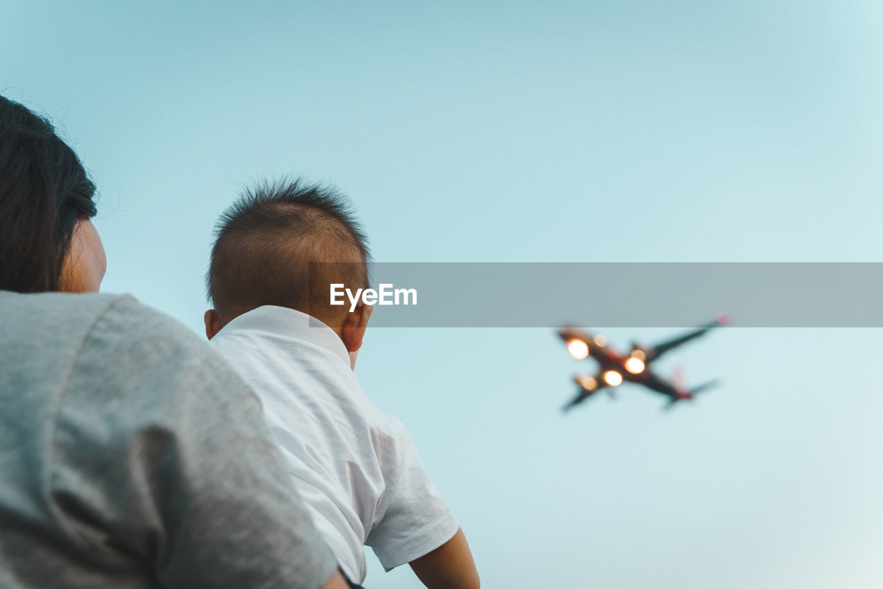 Rear view of young boy and airplane flying against clear sky