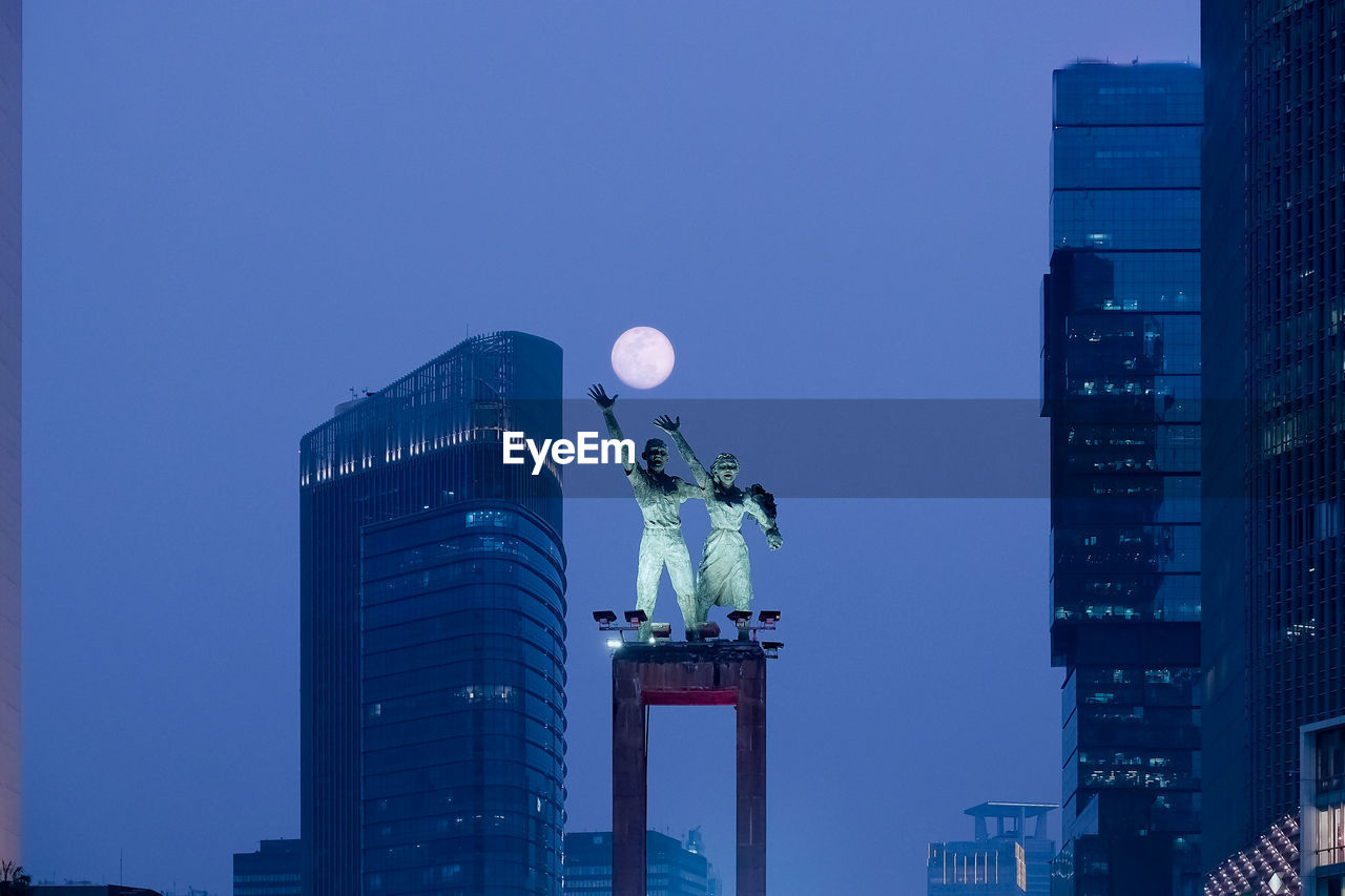 Low angle view of statues against clear sky in city at dusk