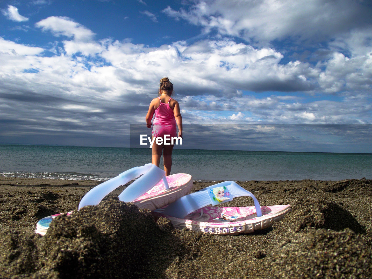 Rear view of girl standing on beach against sky