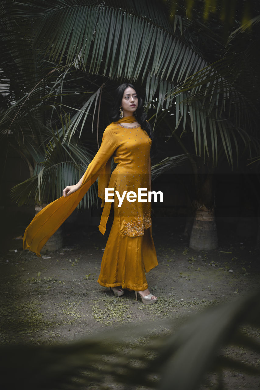 YOUNG WOMAN STANDING BY TREE