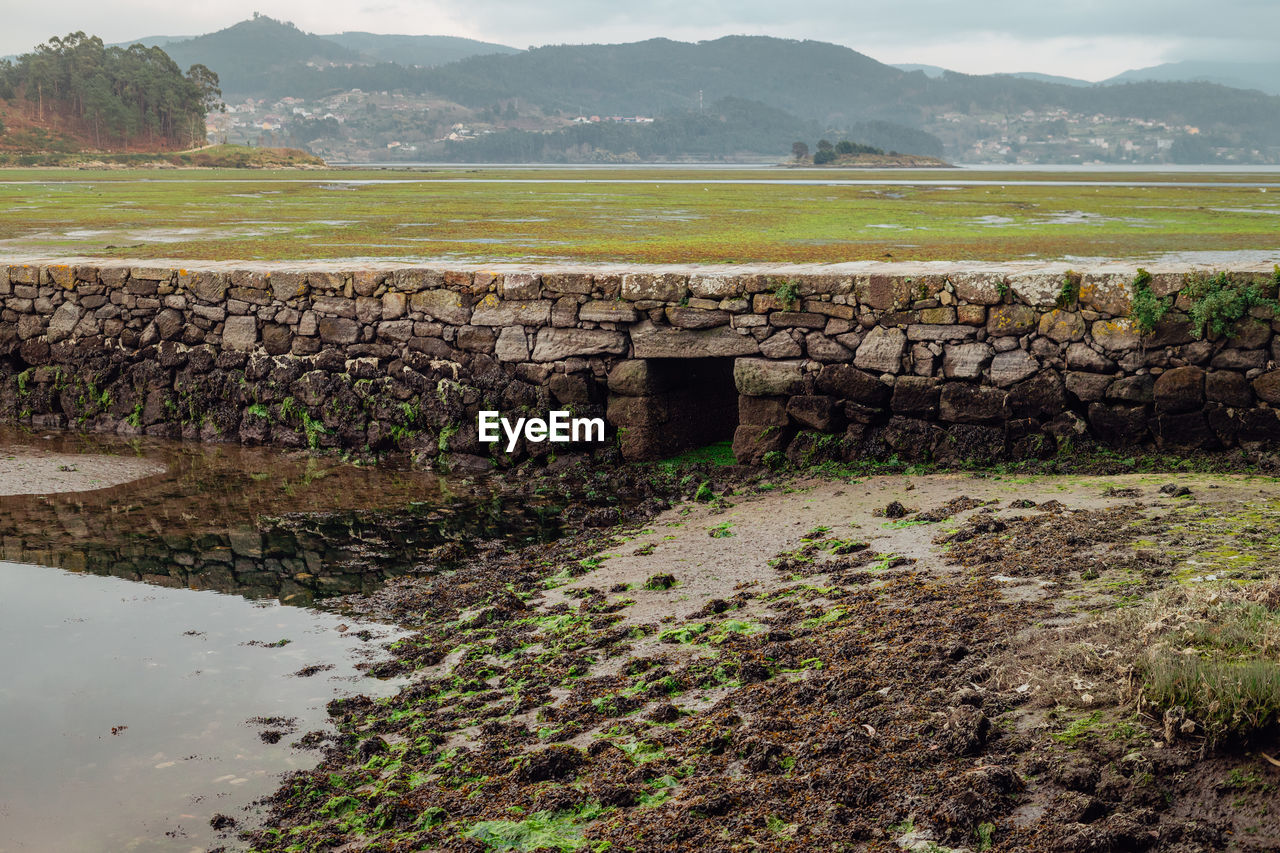 water, rural area, environment, landscape, sea, nature, coast, mountain, land, architecture, sky, reservoir, scenics - nature, no people, shore, rural scene, plant, travel, agriculture, built structure, mountain range, outdoors, travel destinations, soil, social issues, beauty in nature, tranquility, field, cloud, wall, history, rock, day, tourism, ruins, stone wall, grass, stone material, non-urban scene