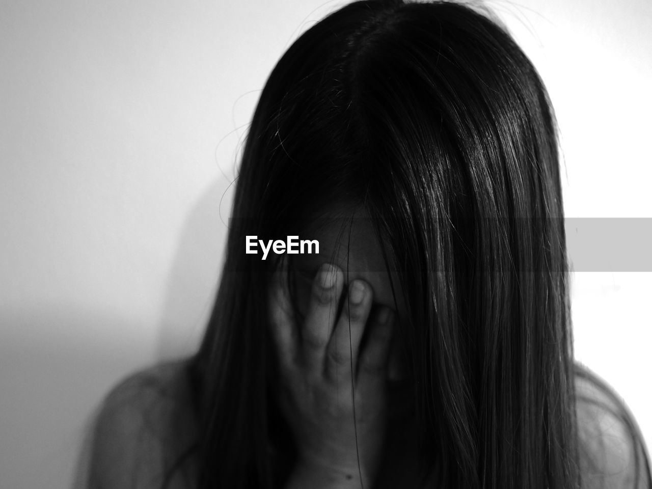 Close-up of depressed woman covering eyes against wall