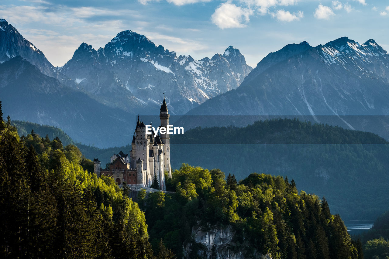 PANORAMIC VIEW OF TREES AND BUILDINGS AGAINST MOUNTAINS