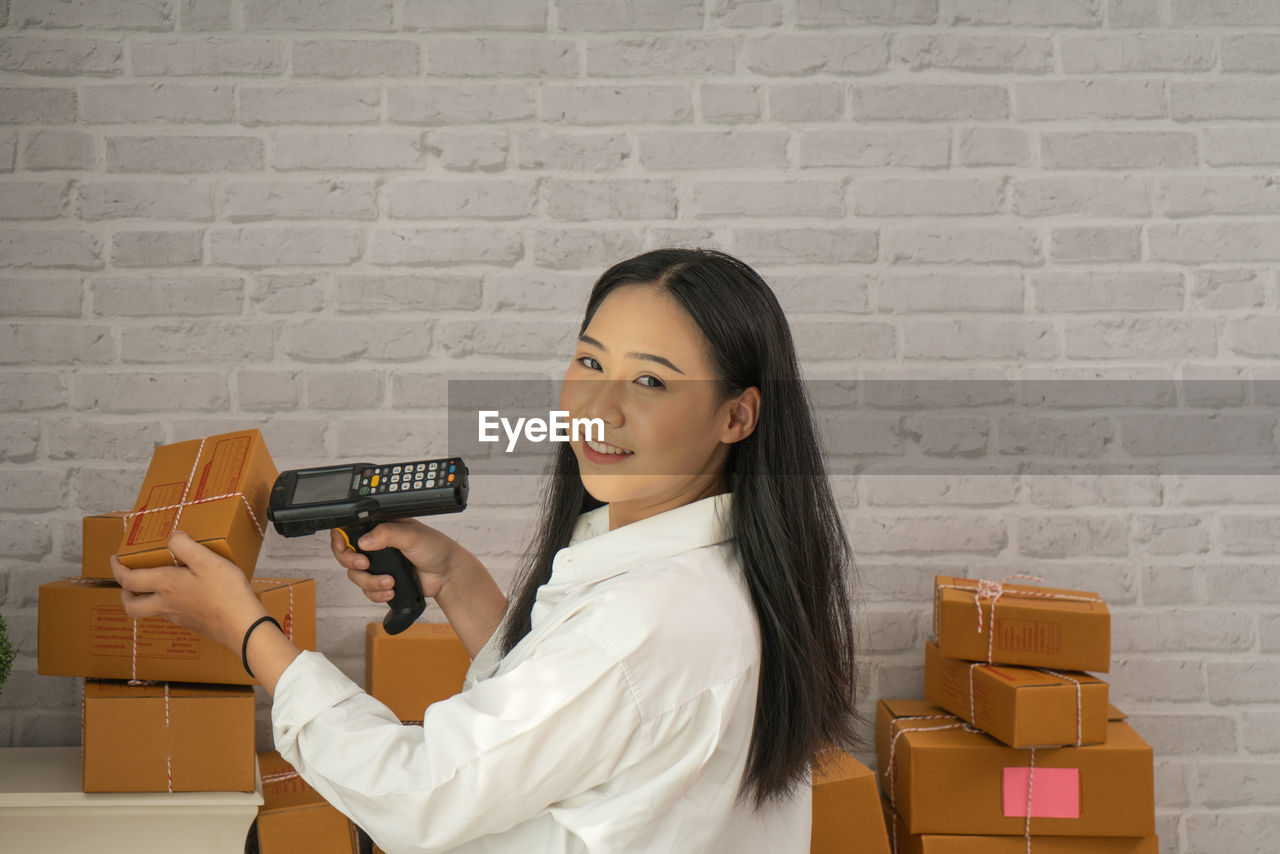 Portrait of businesswoman smiling while using bar code reader on box in office