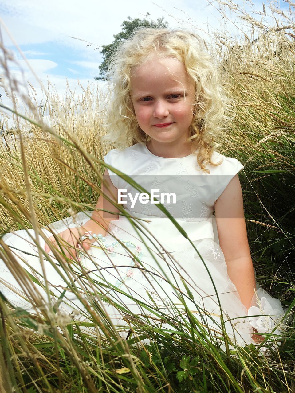 Portrait of cute smiling girl sitting amidst grass on field