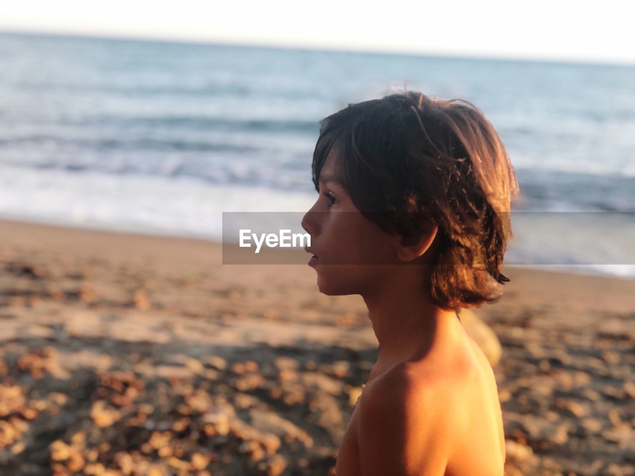 Profile view of thoughtful shirtless boy standing at beach