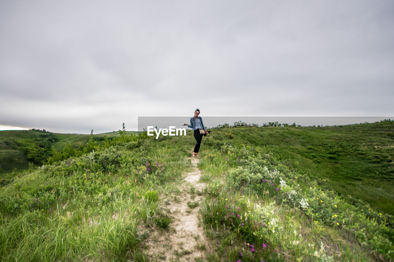 Happy young woman standing on grassy field against cloudy sky at glenbow ranch provincial park