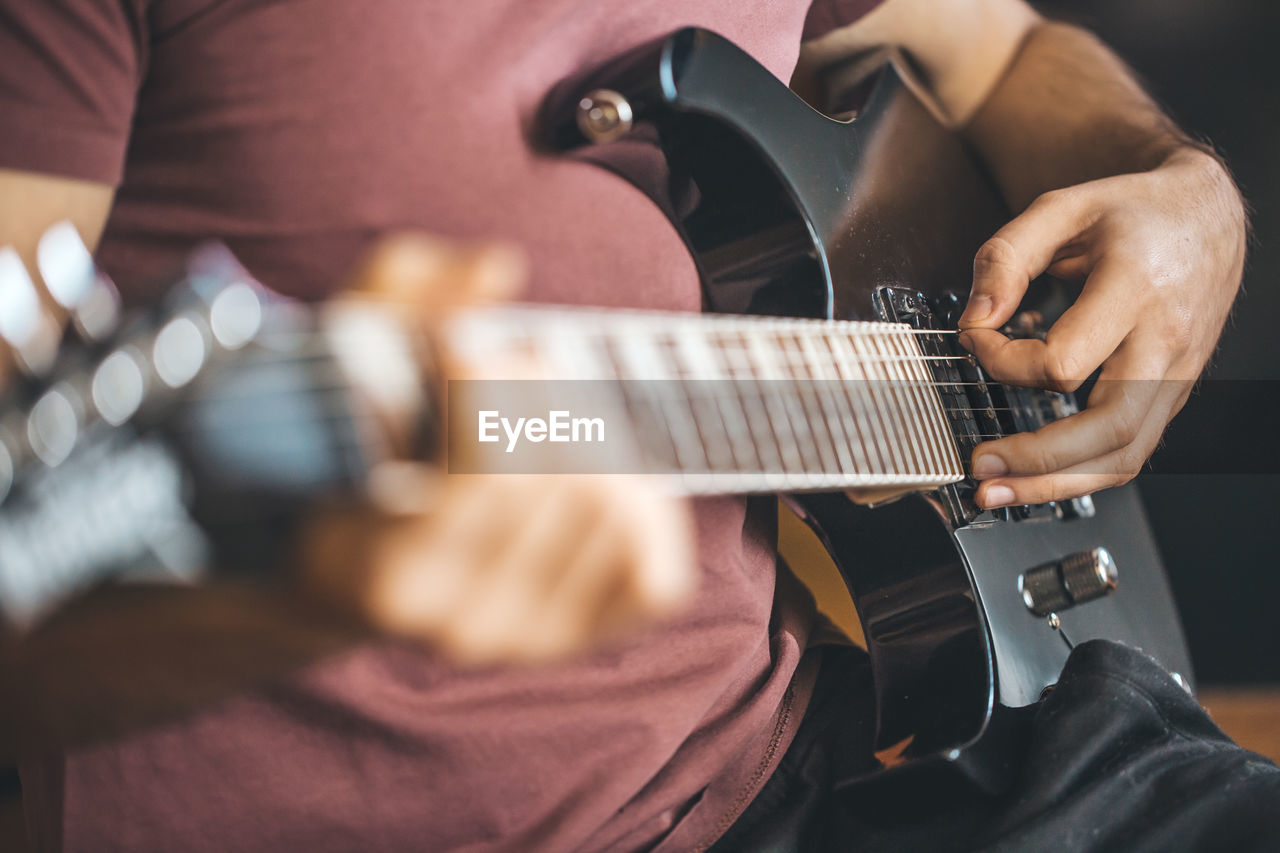 MIDSECTION OF MAN PLAYING GUITAR AT MUSIC