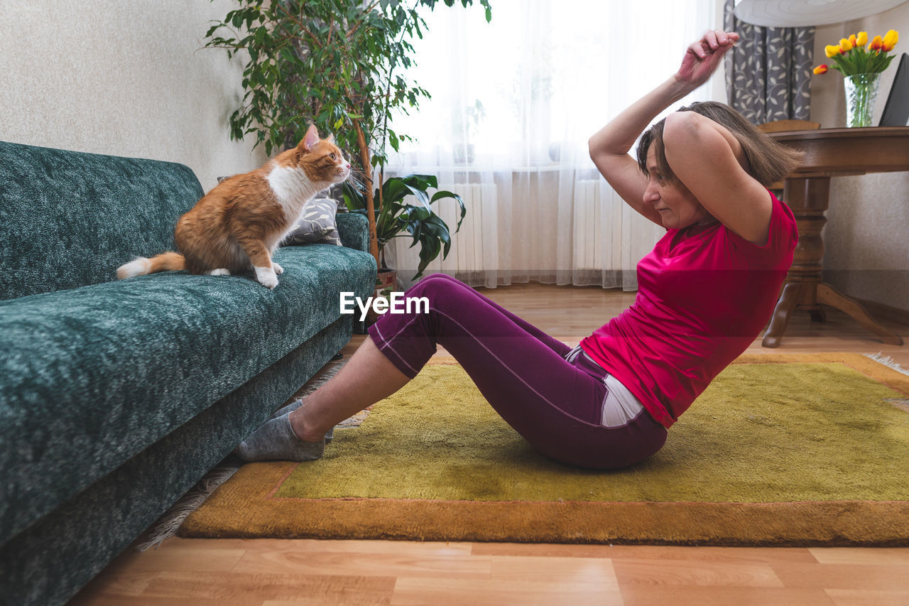A mature woman  doing abdominal exercises at home during the coronavirus pandemic. cat sits near her