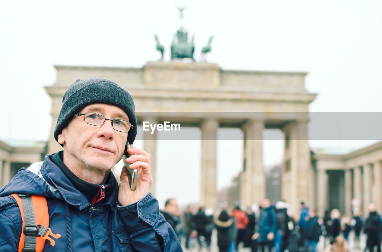 Portrait of man talking on phone against brandenburg gate